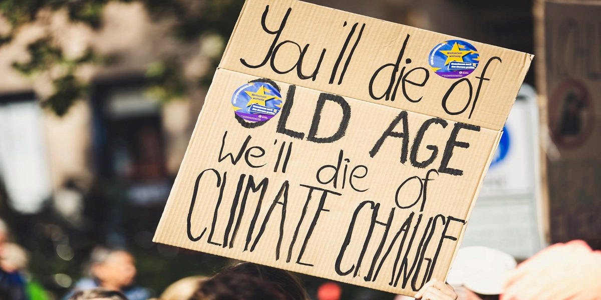 A close-up of a placard reading 'you'll die of old age, we'll die of climate change'