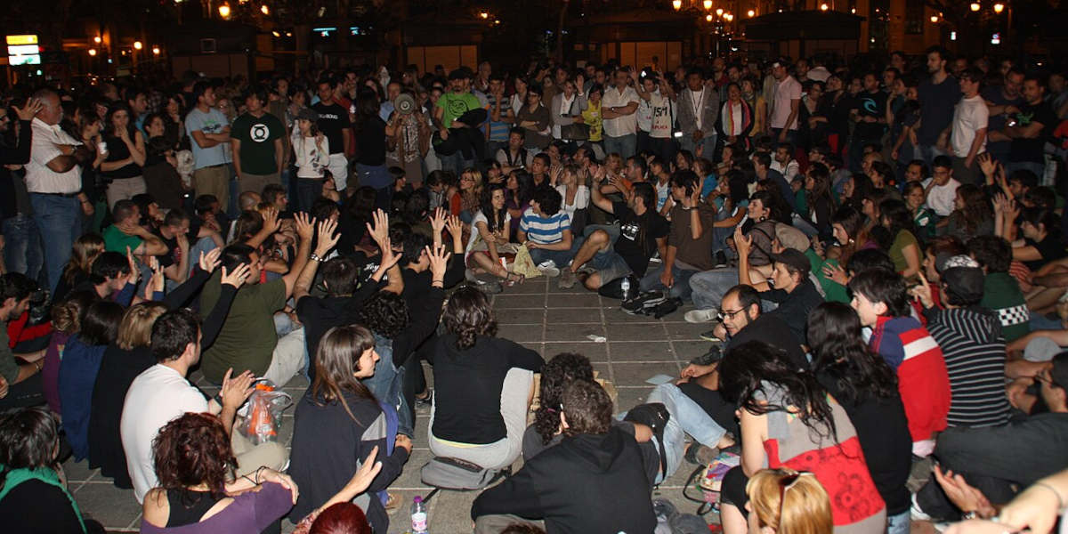 A large group of people sat in a circle at night as part of a group debate, with some raising their hands