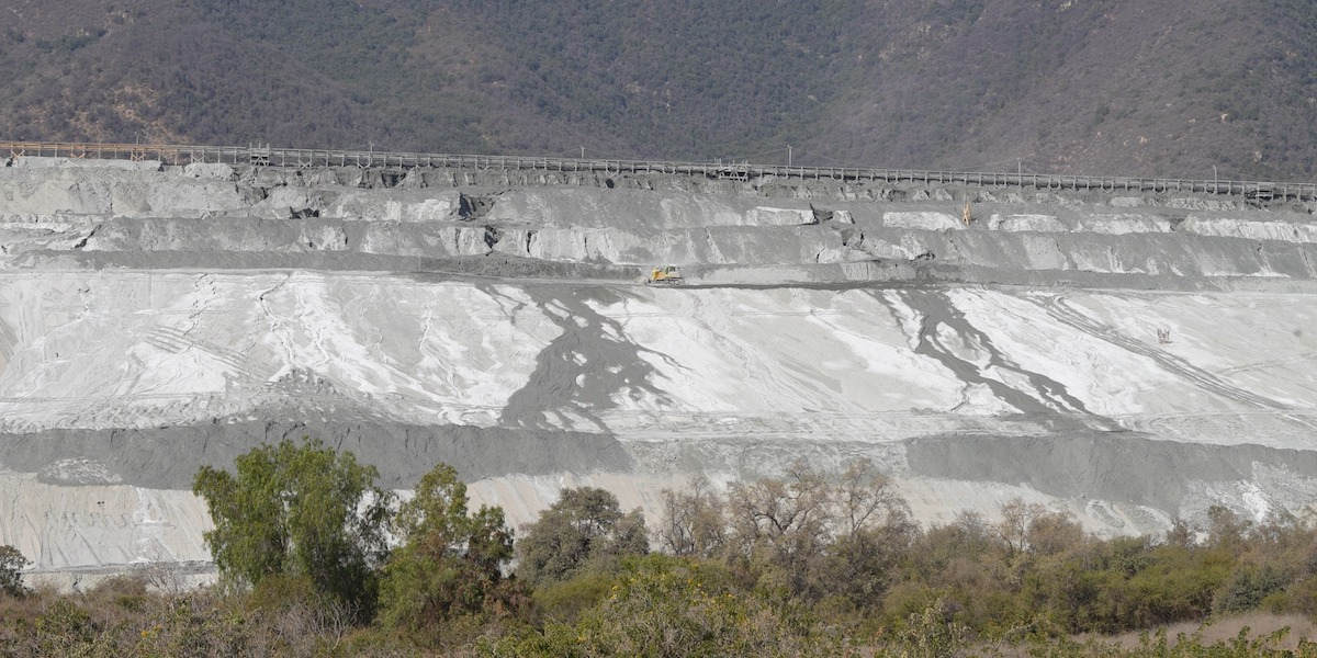 A photo at a distance of a tailings dam, showing large deposits of mining byproducts with a digger in the centre of the photo