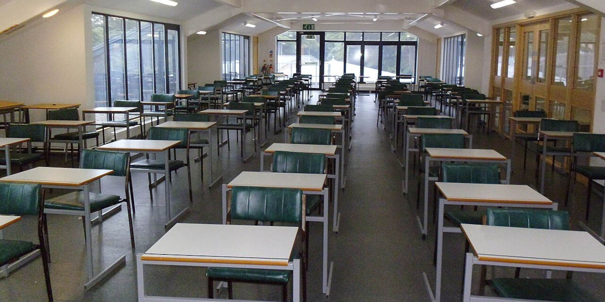 Rows of empty chairs and desks in an empty hall being used for exams