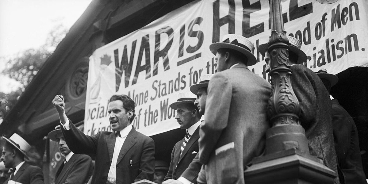 A black and white photograph of Judge and Socialist Party of America activist Jacob Panken, with his fist raised, speaking at an anti-war rally, with a sign behind him reading 'war is hell'