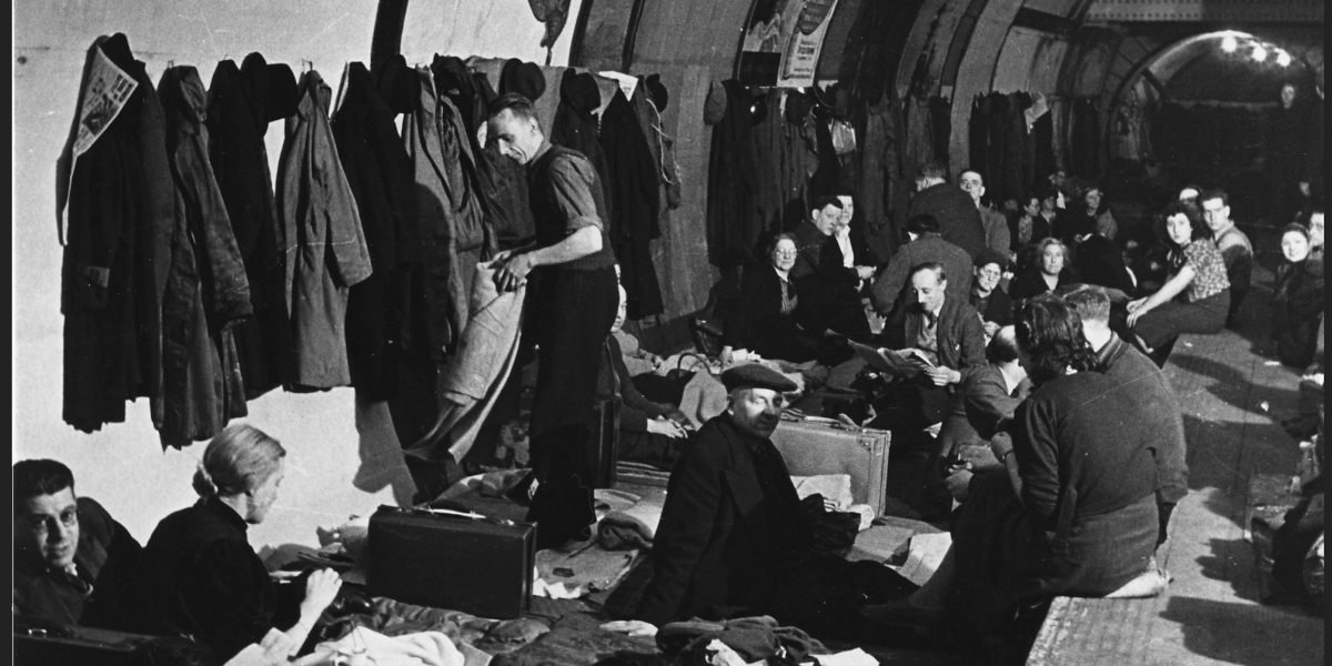 A black and white photograph of several people and their belongings sheltering in the London Underground during the Second World War