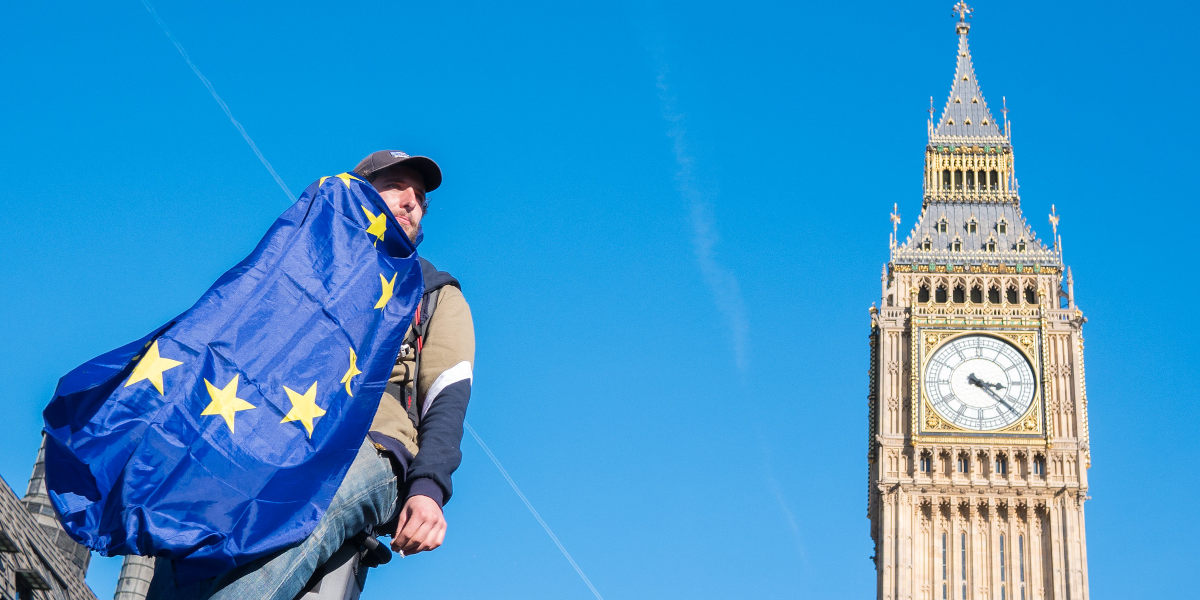 A man at a pro-EU protest holding a European Union flag photographed against a blue sky, with Big Ben in the background