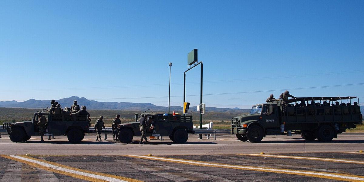 Three vehicles full of Mexican troops silhouetted against a blue sky