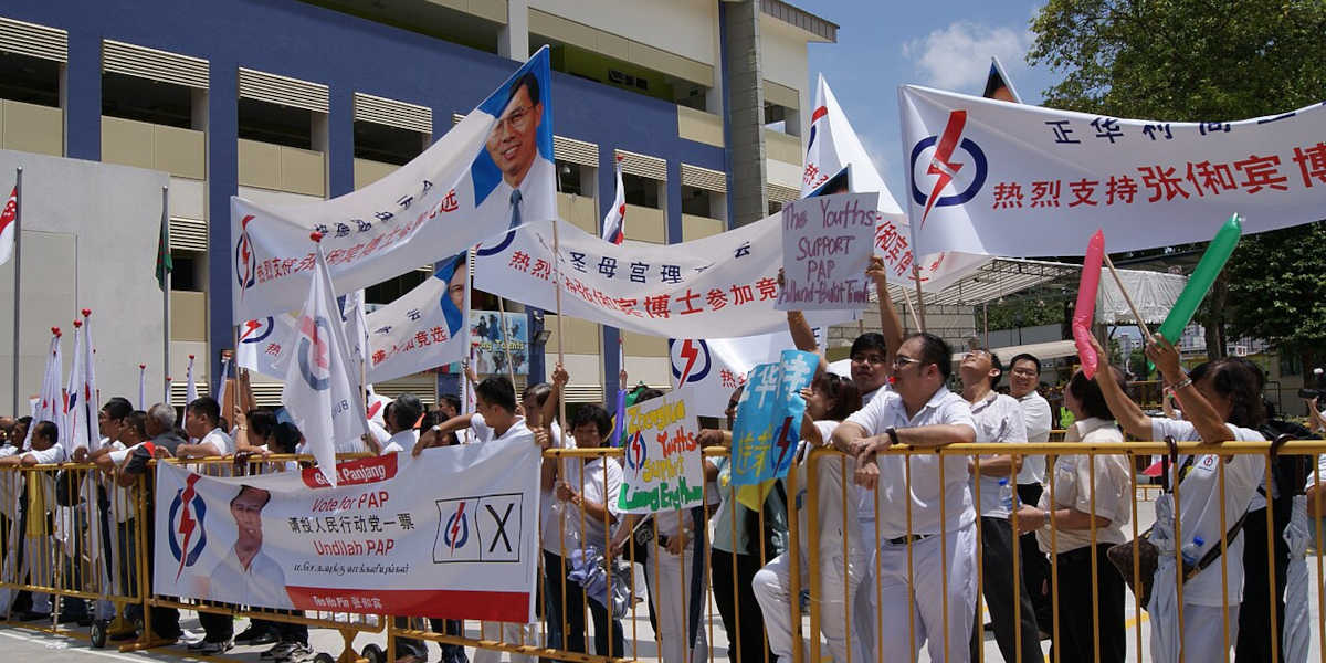 A rally for the People's Action Party, with a large number of people behind a metal barrier holding signs bearing the party's logo