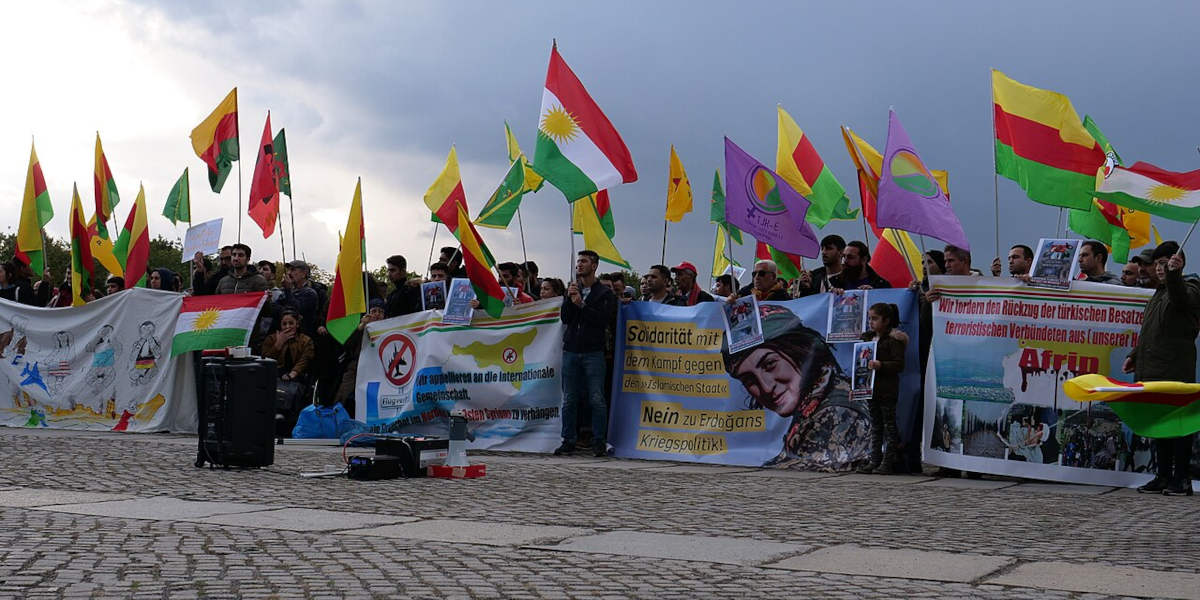A row of protestors at a demonstration in solidarity with Rojava, waving Kurdish flags and holding banners expressing support