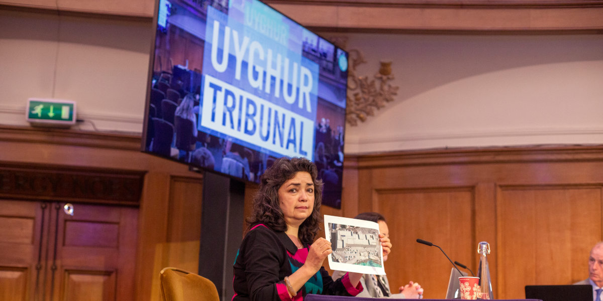 A woman holding a photo of a camp used by China to detain Uyghur prisoners