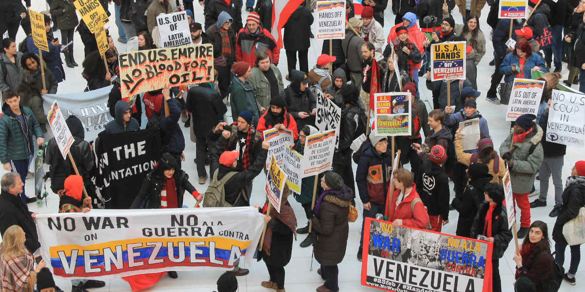 A top-down photo of protestors against US sanctions against Venezuela with placards and signs bearing slogans like, 'No war on Venezuela' and 'End US Empire - No Blood for Oil'