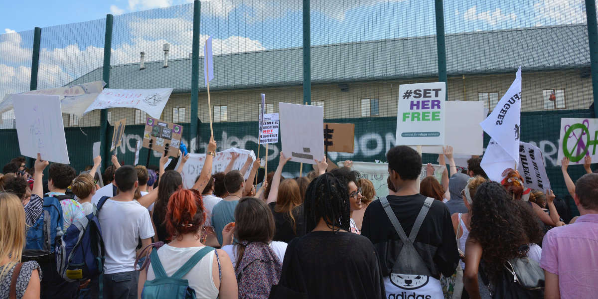 Protestors outside the fence of Yarl's wood immigration detention centre, holding signs and placards expressing solidarity with detained migrants